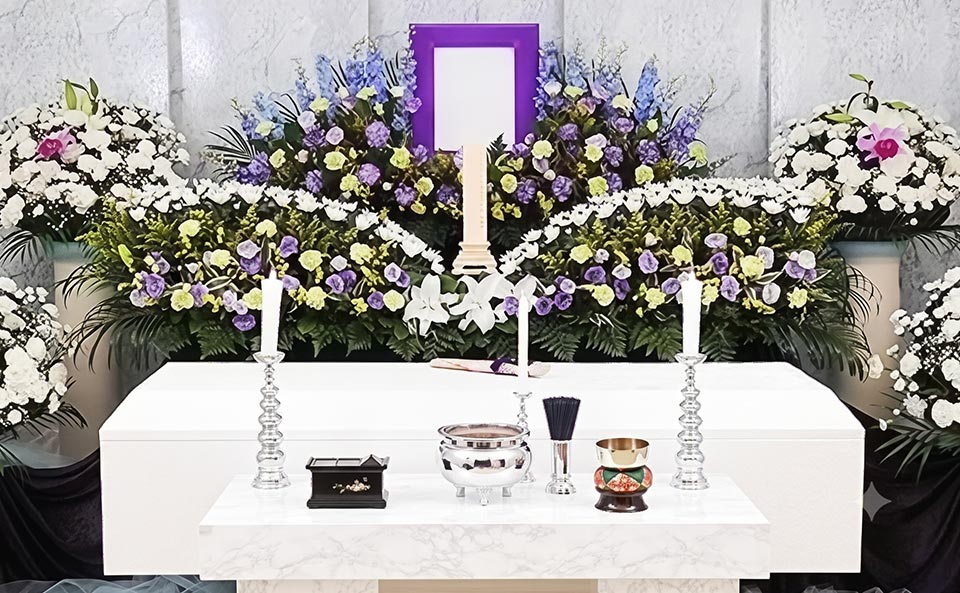 家族葬プランの参考イメージ。紫や白、黄色、青などの生花が飾られた祭壇。中央には遺影額が置かれ、手前には仏具が並んでいます。