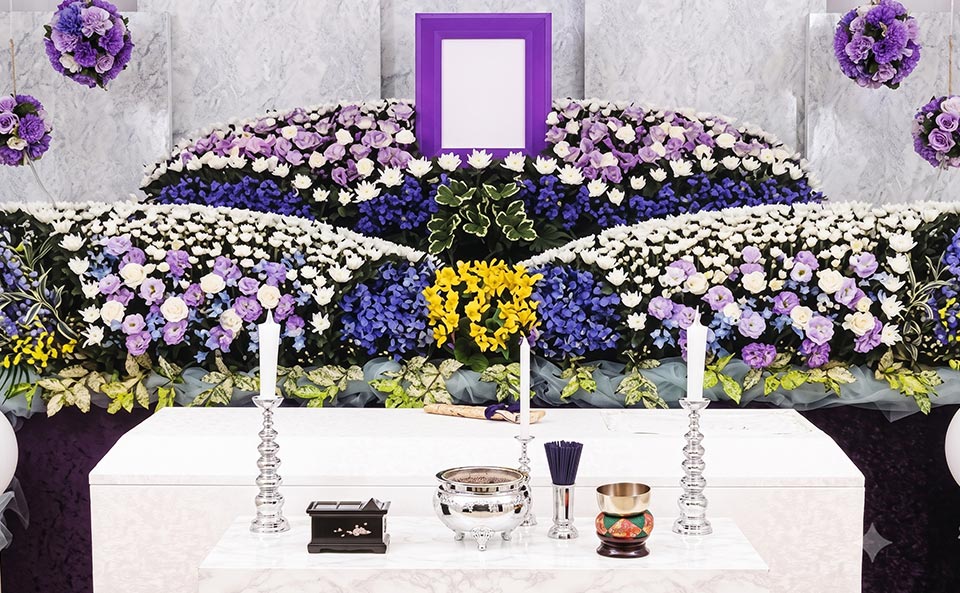 一般葬プランの参考イメージ。紫や白、青、黄色などの色鮮やかな生花が飾られた祭壇。中央には遺影額が置かれ、手前には仏具が並んでいます。